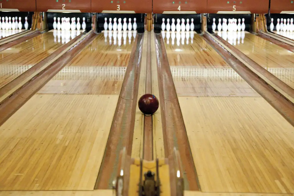 Bowling alley lane with a ball rolling toward the pins.