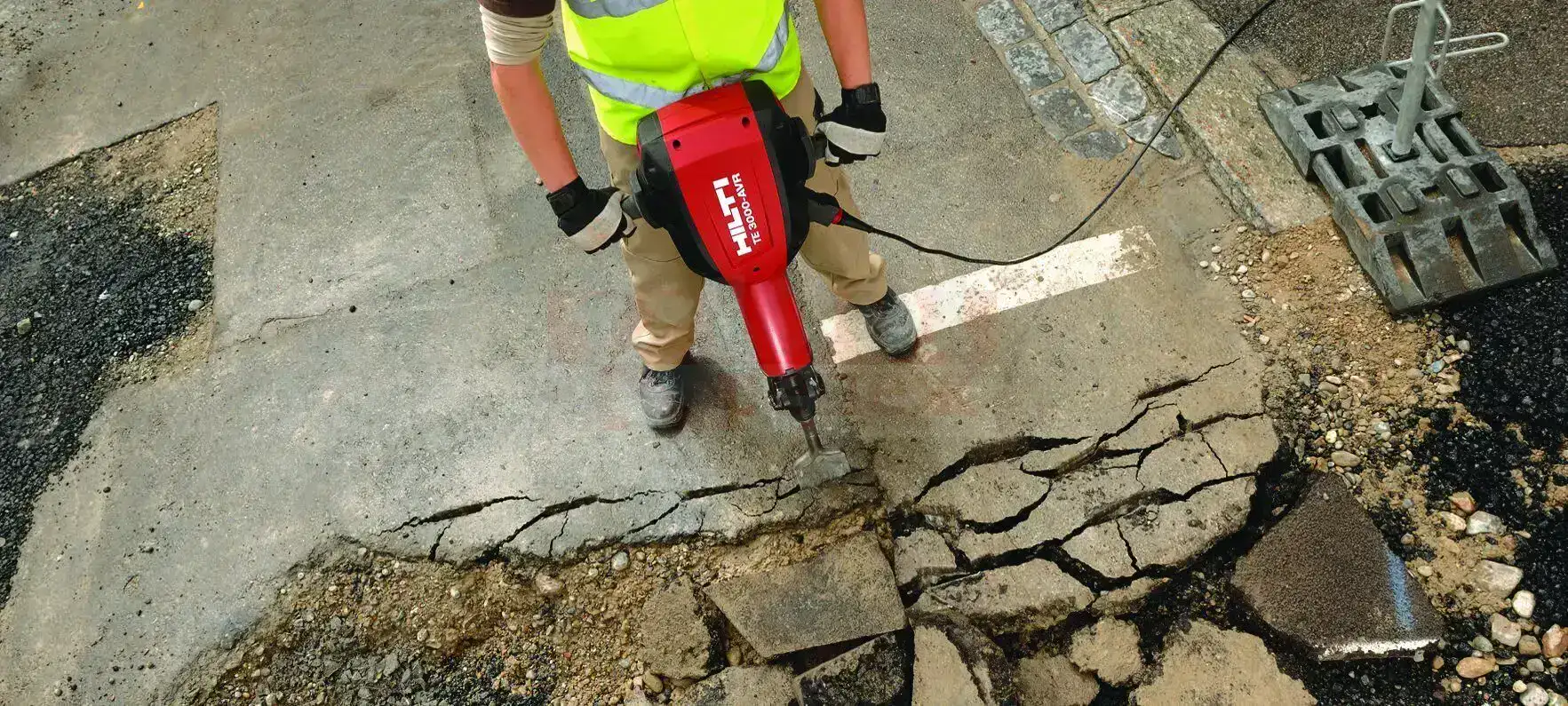 A worker using a powerful jackhammer to break up concrete for removal.