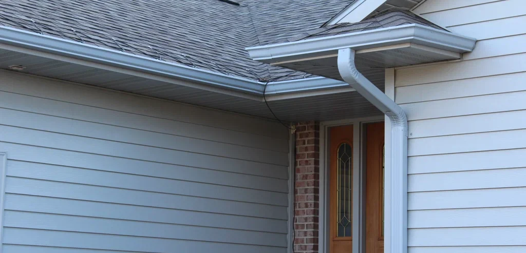 Close-up of a house with aluminum seamless gutters installed, featuring a sloped roof and downspouts.