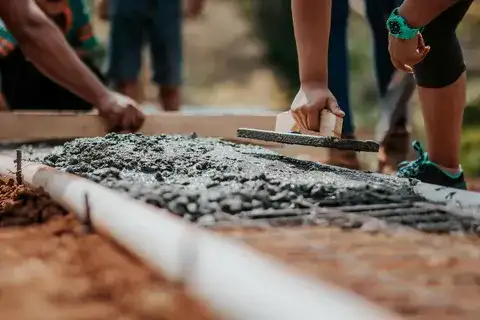 Workers smoothing and leveling freshly poured concrete for a driveway under construction.