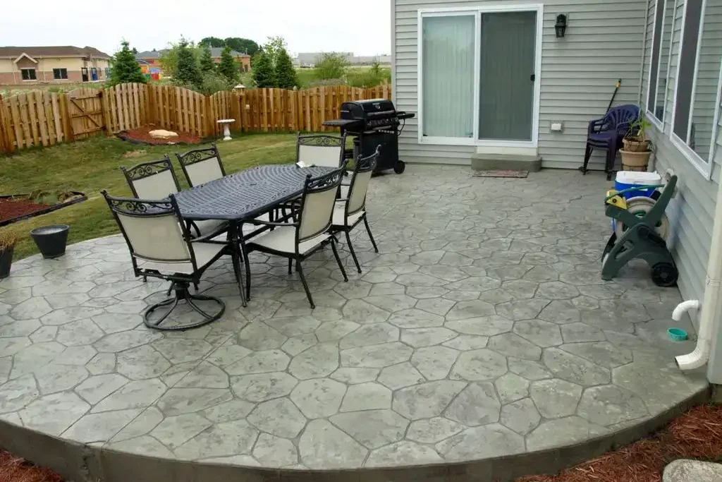 Stamped concrete patio with outdoor dining furniture in a fenced backyard.