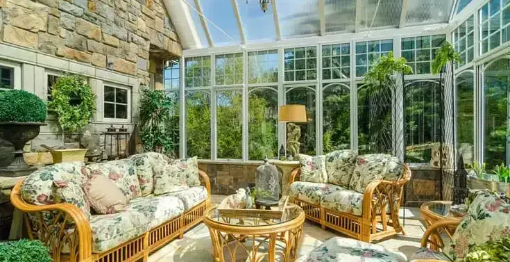 Bright conservatory with glass walls, wicker furniture, and floral decor.