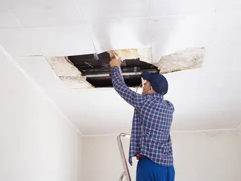 A man repairing ceiling drywall, showcasing home improvement skills and attention to detail.