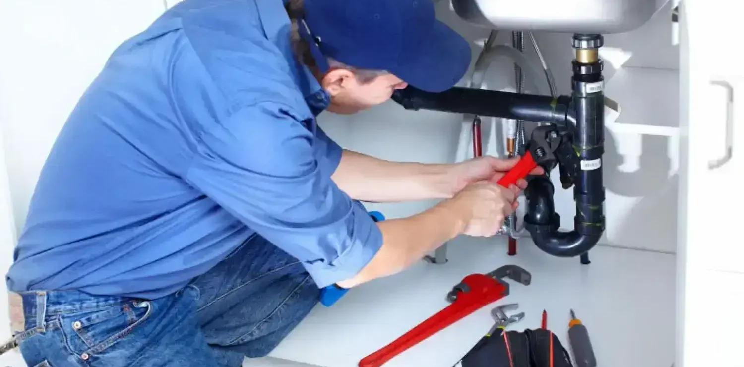 Plumber fixing a kitchen sink pipe with tools nearby.