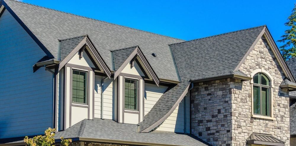 A house featuring a gray roof and green shutters, showcasing a recent roof remodeling project.