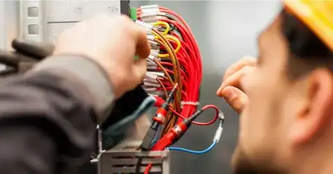 Electrician installing electrical outlets and managing wires in a control panel.