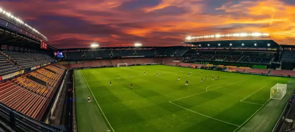 Football stadium at sunset with players on the field and illuminated stands