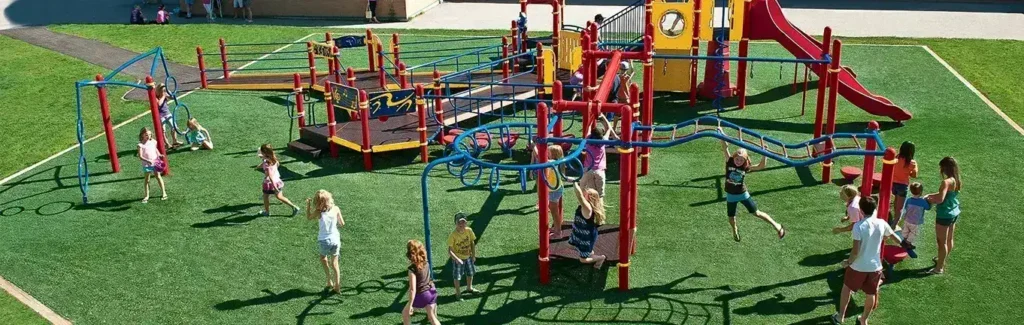 Children playing on colorful playground equipment in a grassy outdoor area.