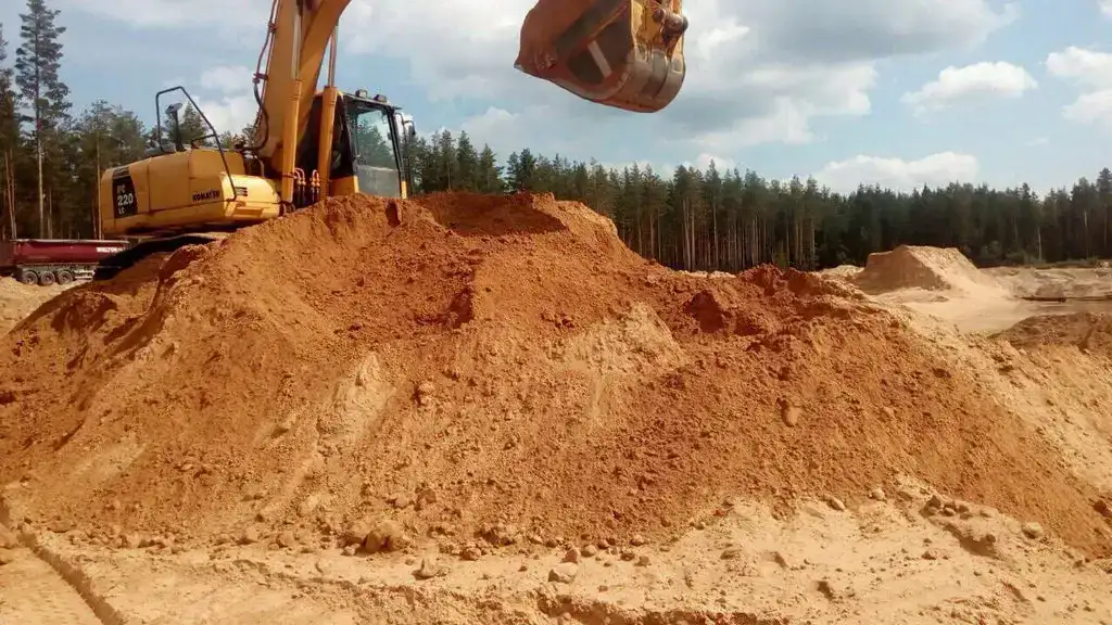 Excavator loading a pile of sand at a construction site.