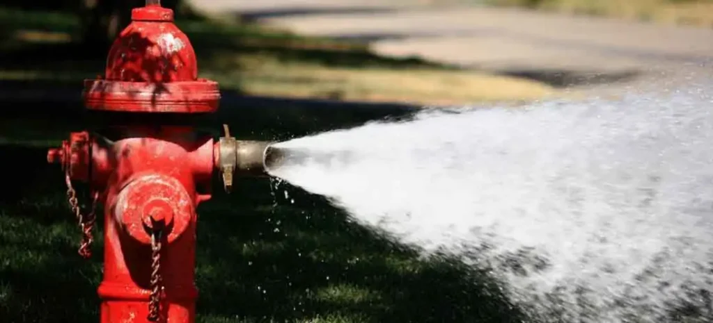 Fire hydrant releasing a strong stream of water outdoors on a sunny day.